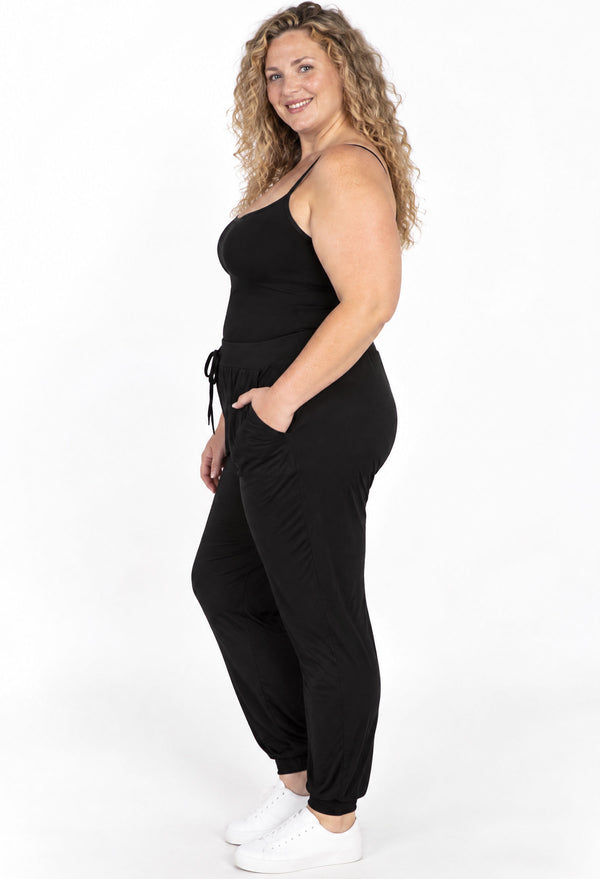 Side profile of curvy model in black bamboo cami and travel pants, showing the high rise and stretchy fit